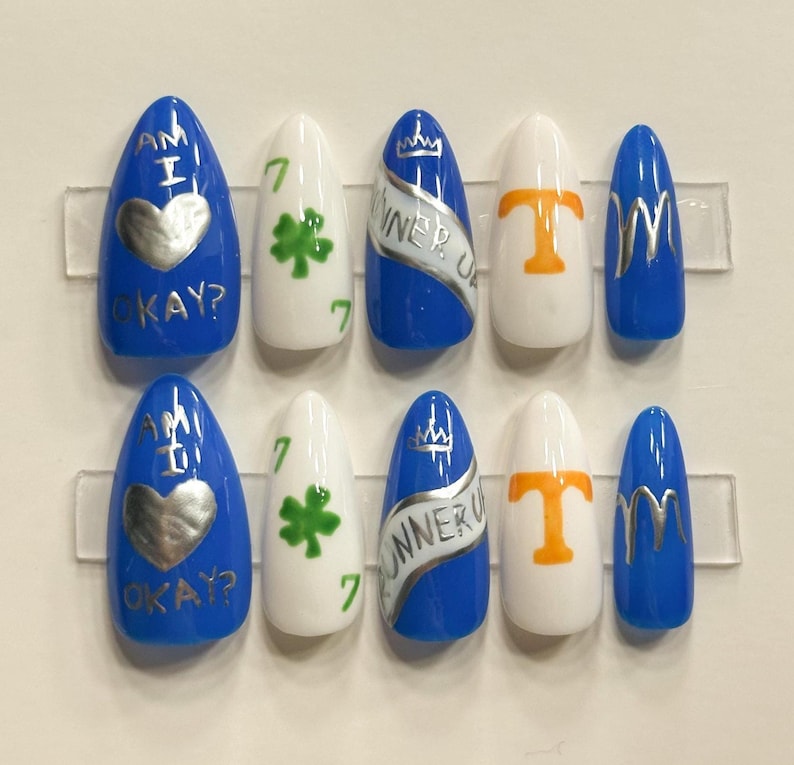 May include: A set of ten artificial nails in various designs. The nails are blue, white, and silver, with text and graphics including a heart, shamrock, and the words "WINNER UP".