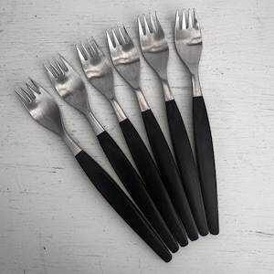 May include: A set of six stainless steel forks with black handles. The forks have a classic design, with tines and a polished finish. The black handles provide a contrast to the silver metal.