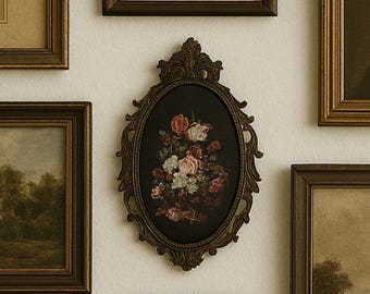 May include: A collection of framed art pieces in various sizes and styles. The central piece is an oval frame with a floral still life painting. Other frames contain landscape and architectural prints, all with dark brown frames.