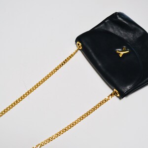 May include: A black leather shoulder bag with a gold chain strap and a gold accent on the flap.