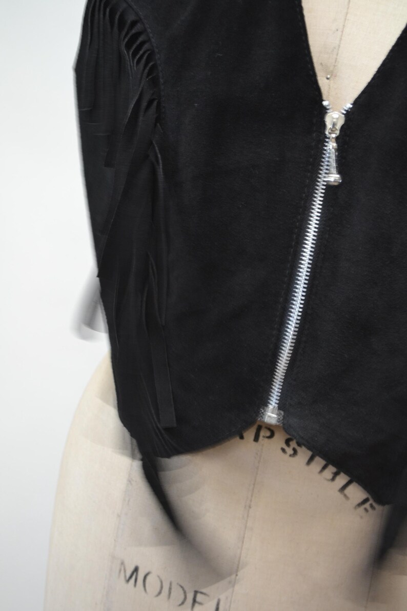 May include: Black suede vest with fringe detailing and a zipper closure.