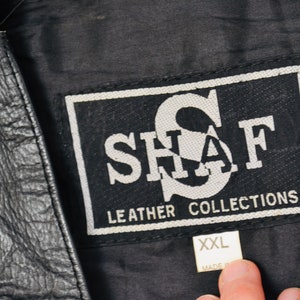 K&ouml;nnte beinhalten: Schwarze Lederjacke mit einem wei&szlig;en Etikett mit der Aufschrift "SHAF LEATHER COLLECTIONS" und einem wei&szlig;en Gr&ouml;&szlig;enetikett mit der Aufschrift "XXL".