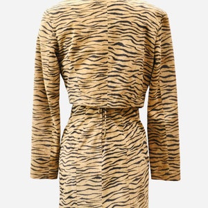 Op de afbeelding: Een tan en zwart tijgerprintjurk met een bijpassend jasje. De jurk heeft een aansluitende pasvorm en een riem in de taille. Het jasje heeft lange mouwen en een kraag.
