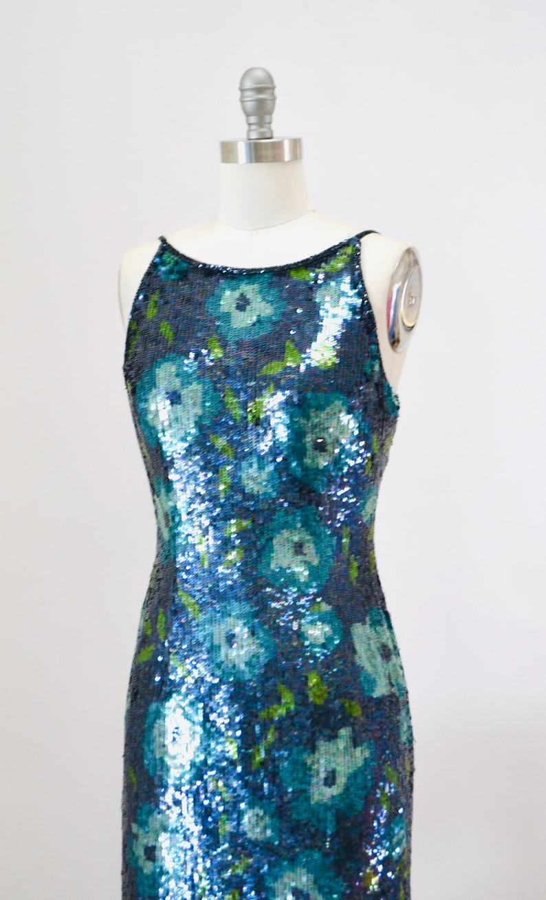 May include: A sleeveless sequined dress with a floral pattern in shades of blue and green.