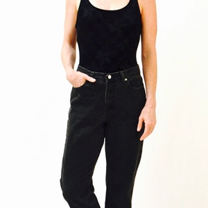 May include: A woman wearing a black tank top and black jeans with a cuffed hem. She is wearing black sandals with gold embellishments.
