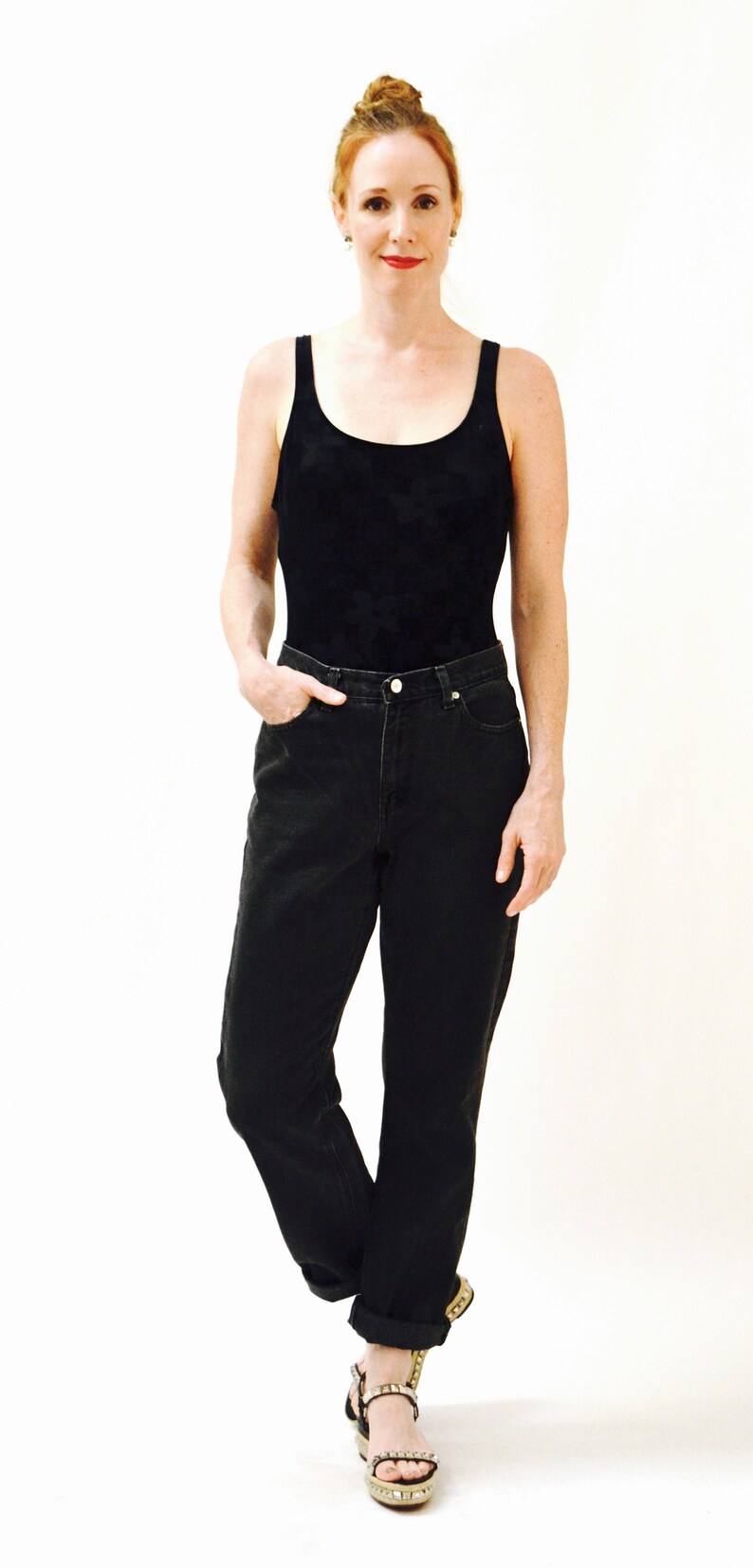 May include: A woman wearing a black tank top and black jeans with a cuffed hem. She is wearing black sandals with gold embellishments.