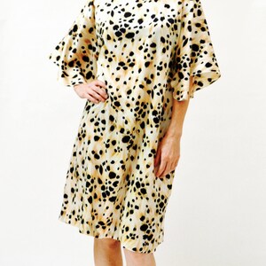 May include: A woman wearing a white dress with a black and brown animal print. The dress has a loose fit and short sleeves. She is wearing sandals with rhinestones.