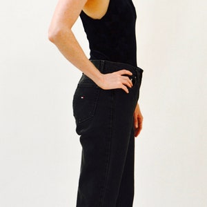May include: A woman wearing a black tank top and dark wash jeans with a cuffed hem. She is wearing black sandals with silver studs.