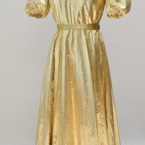 May include: A gold metallic dress with a V-neckline and short puff sleeves. The dress has a beaded embellishment around the neckline and a gold belt.