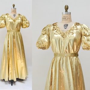 May include: A gold metallic dress with a V-neckline, puff sleeves, and a gold belt. The dress has a flowing skirt and is made of a shiny fabric.