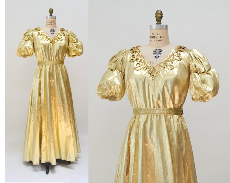 May include: A gold metallic dress with a V-neckline, puff sleeves, and a gold belt. The dress has a flowing skirt and is made of a shiny fabric.