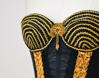 May include: A black strapless corset with gold embroidery and sequins. The corset has a sweetheart neckline and a boned bodice.