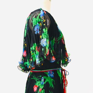 May include: A black maxi dress with a floral print in shades of green, blue, red, and yellow. The dress has a pleated skirt and a tie at the waist.