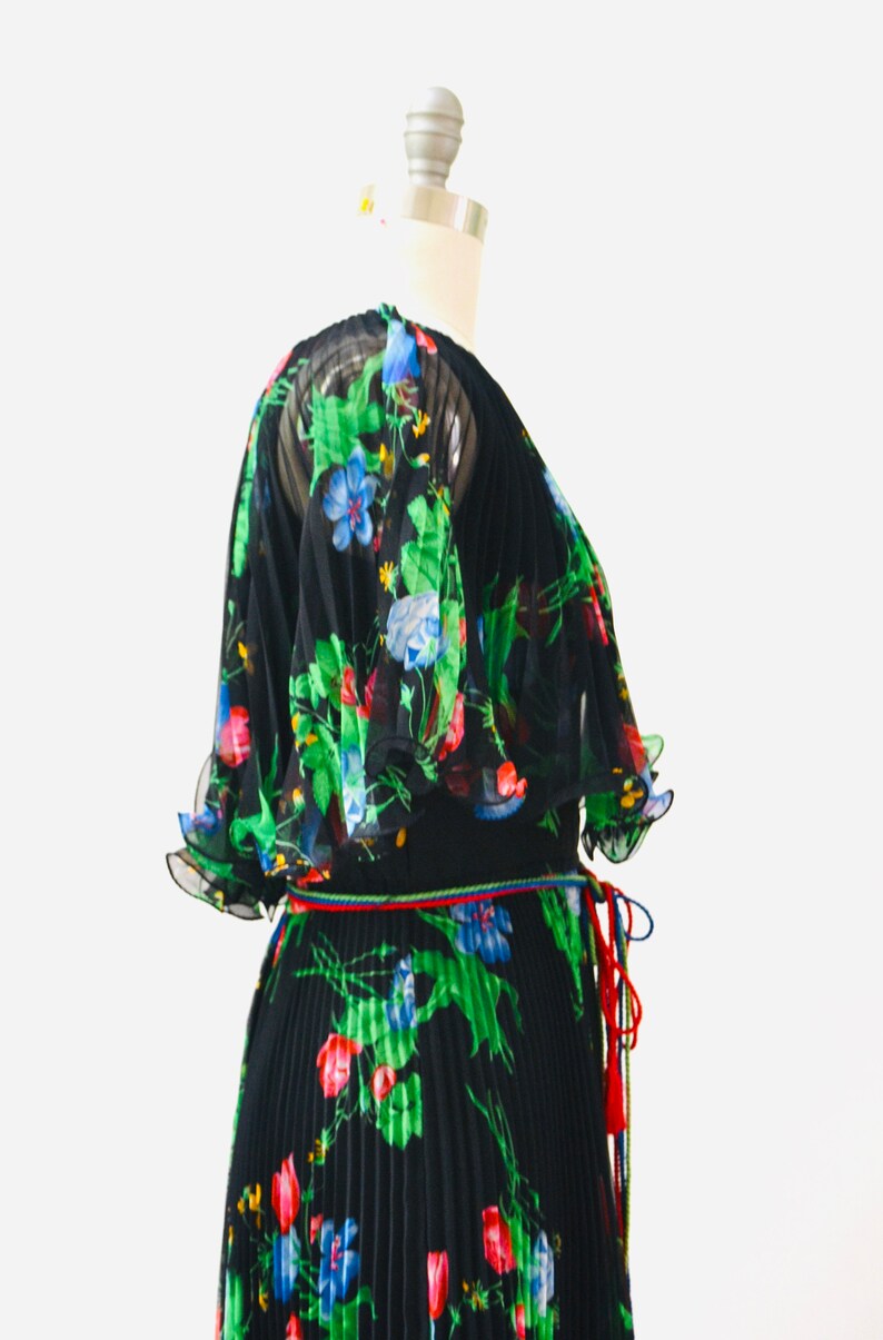 May include: A black maxi dress with a floral print in shades of green, blue, red, and yellow. The dress has a pleated skirt and a tie at the waist.