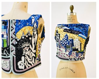 May include: A sleeveless top with a colorful, beaded design featuring the Statue of Liberty and the words "New York".