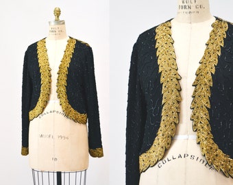 May include: A black cropped jacket with gold leaf embroidery. The jacket has a V-neck and long sleeves.