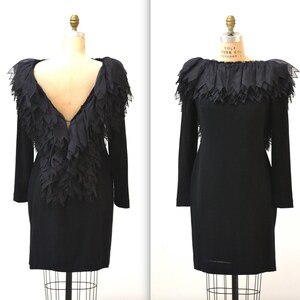 May include: A black dress with a ruffled neckline and a deep V-back. The ruffles are made of a sheer fabric and are layered to create a dramatic effect.