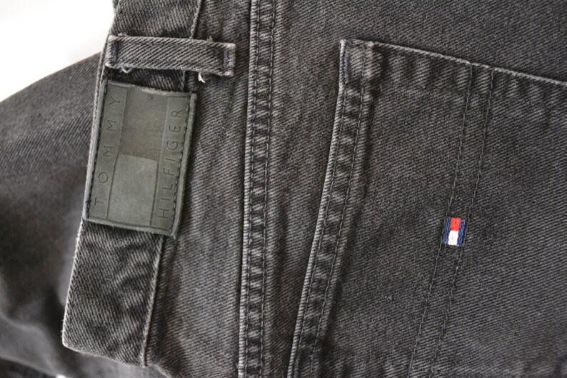 May include: A pair of dark gray denim jeans with a Tommy Hilfiger label and a small red, white, and blue logo patch on the back pocket.