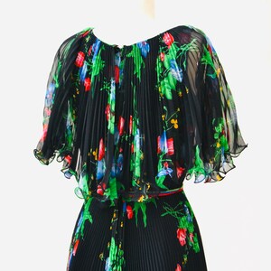 May include: A black pleated maxi dress with a floral print in shades of green, red, blue, and yellow. The dress has a ruffled neckline and short sleeves.