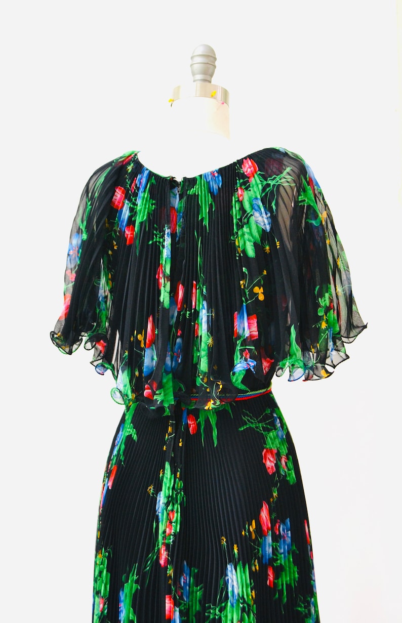 May include: A black pleated maxi dress with a floral print in shades of green, red, blue, and yellow. The dress has a ruffled neckline and short sleeves.
