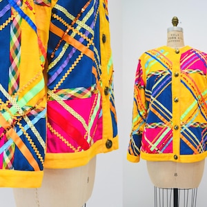 Könnte beinhalten: Eine gelbe, blaue und rosafarbene Jacke mit einem Patchwork-Design aus bunten Bändern. Die Jacke hat einen Knopfverschluss und einen Kragen.