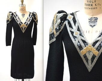 May include: Black knit dress with gold and silver sequins forming a geometric pattern on the shoulders and neckline. The dress has long sleeves and a v-neck.