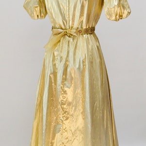 May include: A gold metallic dress with a gathered neckline and short puff sleeves. The dress has a gold beaded belt and a flowing skirt.