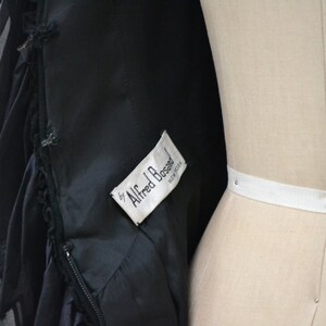 May include: Black dress with a ruffled hem and a white label that reads "by Alfred Bossel, New York".