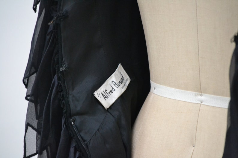 May include: Black dress with a ruffled hem and a white label that reads "by Alfred Bossel, New York".