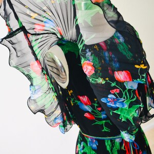 May include: A black sheer dress with a floral print in shades of red, pink, blue, green, and yellow. The dress has a pleated skirt and a ruffled neckline.