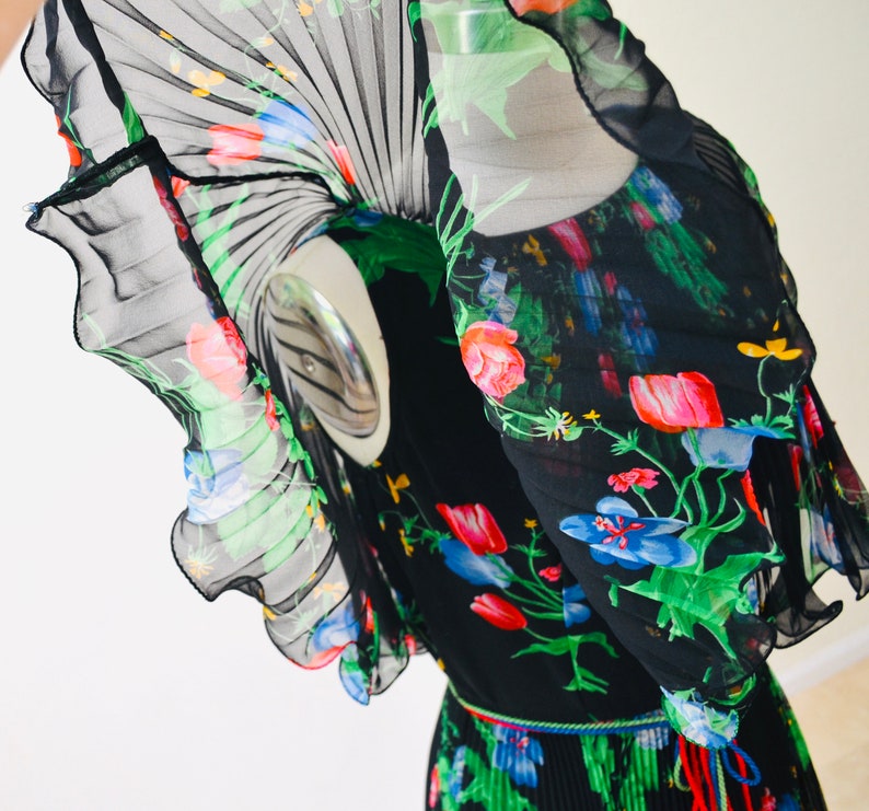 May include: A black sheer dress with a floral print in shades of red, pink, blue, green, and yellow. The dress has a pleated skirt and a ruffled neckline.