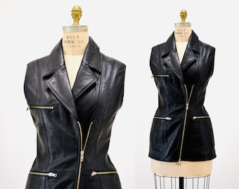 May include: Black leather vest with a zipper closure and multiple pockets. The vest has a collar and is sleeveless. The vest has gold zippers.