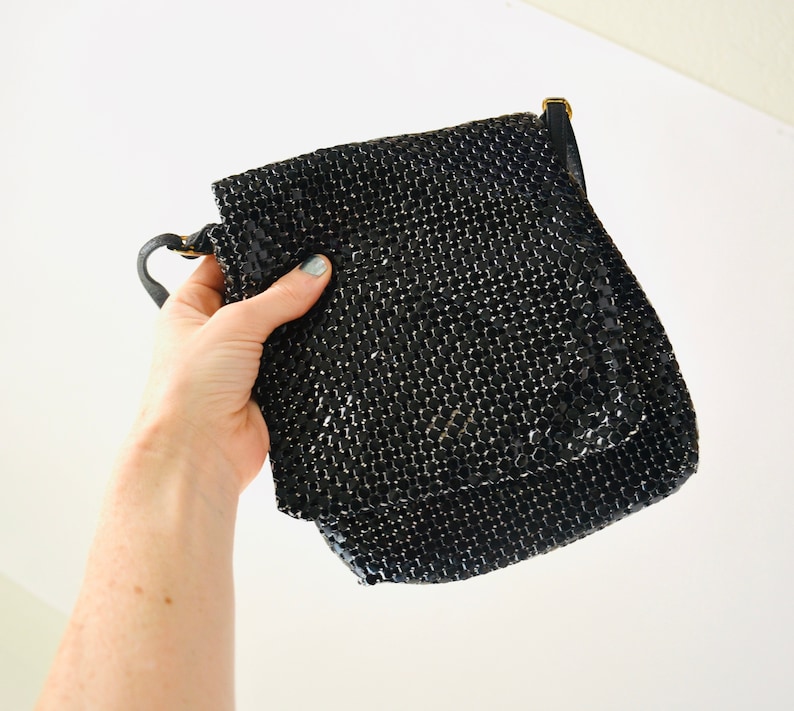 May include: A black mesh chain bag with a short strap. The bag is made of small, shiny, black squares.