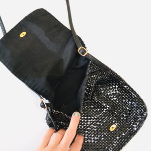 May include: A black sequined evening bag with a flap closure and a gold chain strap. The bag is open and the inside is lined with black fabric.