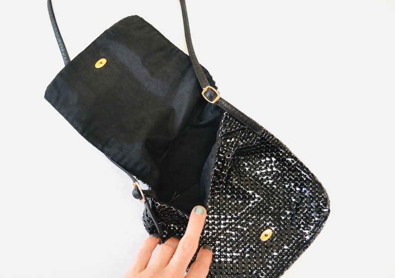 May include: A black sequined evening bag with a flap closure and a gold chain strap. The bag is open and the inside is lined with black fabric.