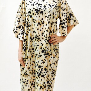 May include: A woman wearing a short-sleeved, knee-length dress with a leopard print pattern. The dress is white with black and brown spots. She is wearing sandals with silver embellishments.
