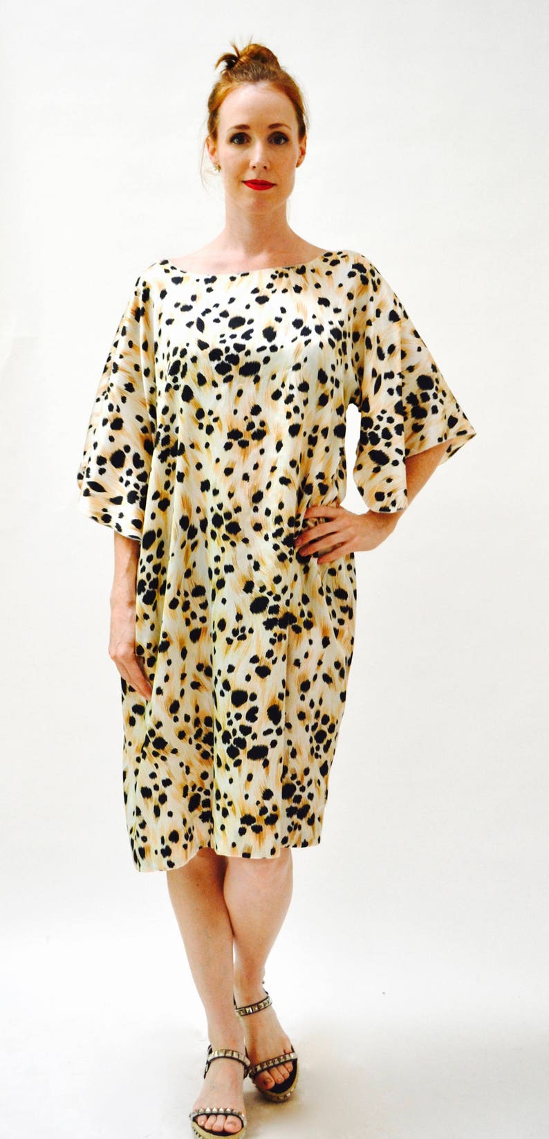 May include: A woman wearing a short-sleeved, knee-length dress with a leopard print pattern. The dress is white with black and brown spots. She is wearing sandals with silver embellishments.