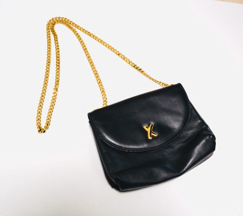 May include: A black leather shoulder bag with a gold chain strap and a gold Y-shaped logo.