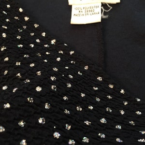 May include: A black top with a V-neckline and a sparkly, textured fabric. The top has a white label with the text "Reggio" and "100% Polyester RN 39960 Made in Sri Lanka".