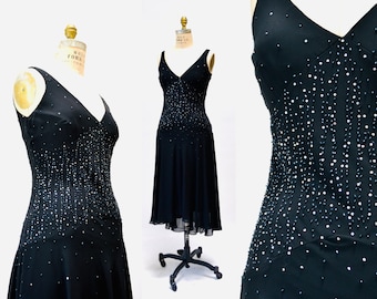 May include: A black sleeveless dress with a V-neckline and a beaded design. The dress has a fitted bodice and a flowing skirt.