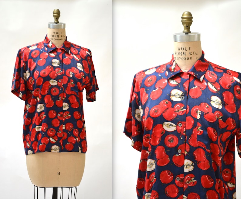 May include: A short-sleeved button-down shirt with a navy blue background and a red apple print. The shirt has a collar and a button-up front.