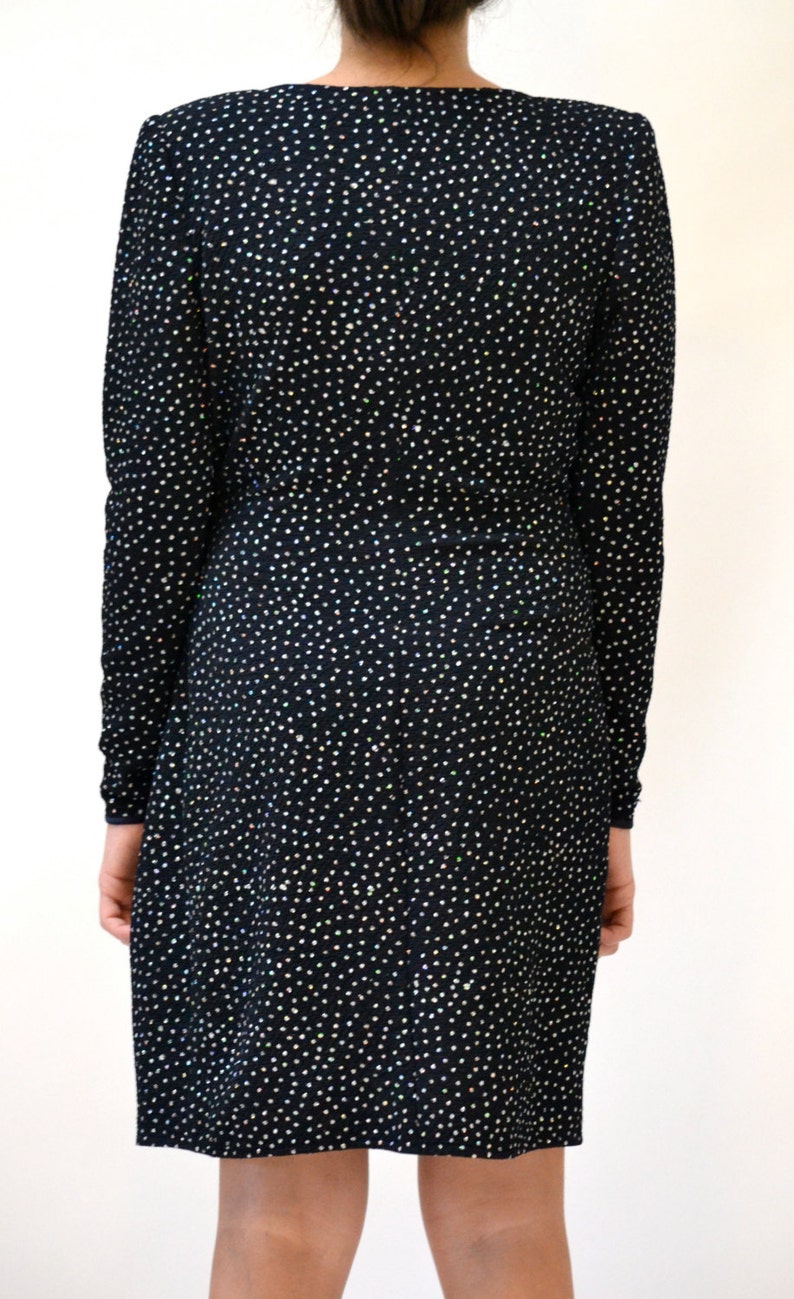 May include: A black long-sleeved dress with a sparkly, all-over pattern. The dress has a V-neckline and a fitted silhouette.