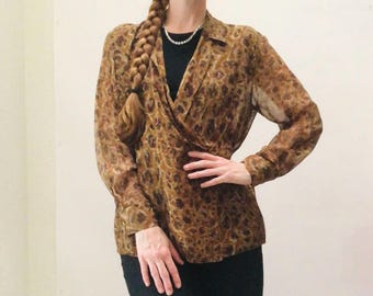 May include: A brown and tan animal print blouse with long sleeves and a wrap-style front. The blouse is paired with a black top and skirt. A woman is wearing the blouse.