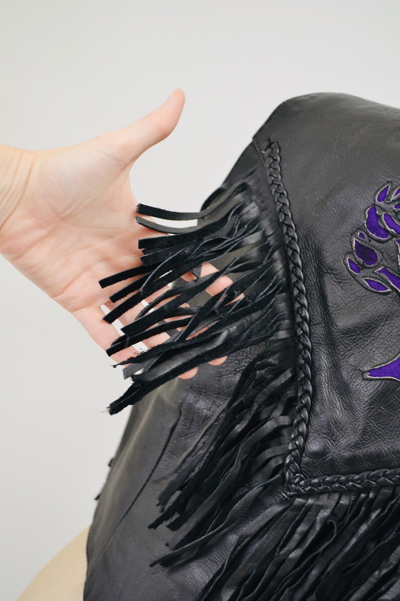K&ouml;nnte beinhalten: Schwarze Lederjacke mit Fransen und einem gestickten Design in Lila. Die Jacke hat einen geflochtenen Besatz an den R&auml;ndern.