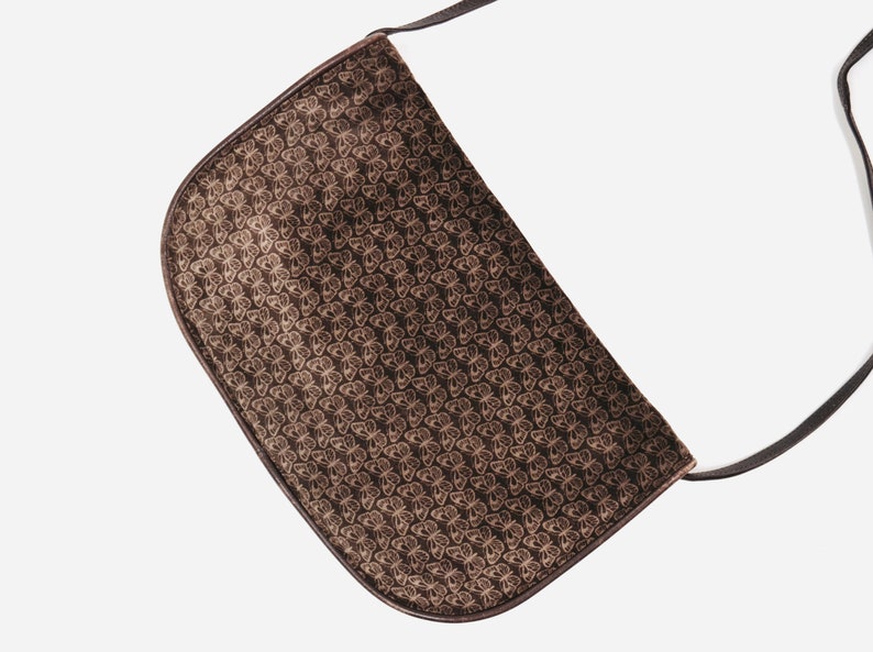 May include: A brown suede shoulder bag with a butterfly pattern. The bag has a long strap and a flap closure.