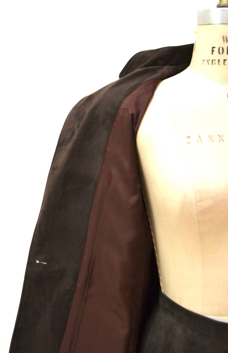 May include: A brown suede coat with a brown satin lining. The coat is open and the lining is visible.