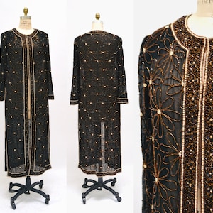 May include: A long, black beaded cardigan with gold accents. The cardigan has a floral pattern and a front closure.