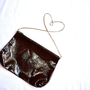 May include: A brown snakeskin clutch bag with a gold chain strap. The chain is shaped into a heart.