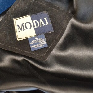 May include: A black leather jacket with a blue lining. The label reads "MODAL" and indicates the jacket is size XL, made in India, with a shell of 100% genuine leather, lining of 100% polyester, and a  RN # 100374.
