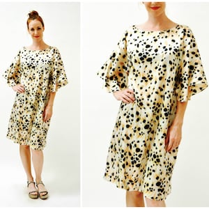 May include: A short-sleeved dress with a beige background and a black and brown animal print. The dress has a round neckline and a loose fit. The sleeves are ruffled and end at the elbow.